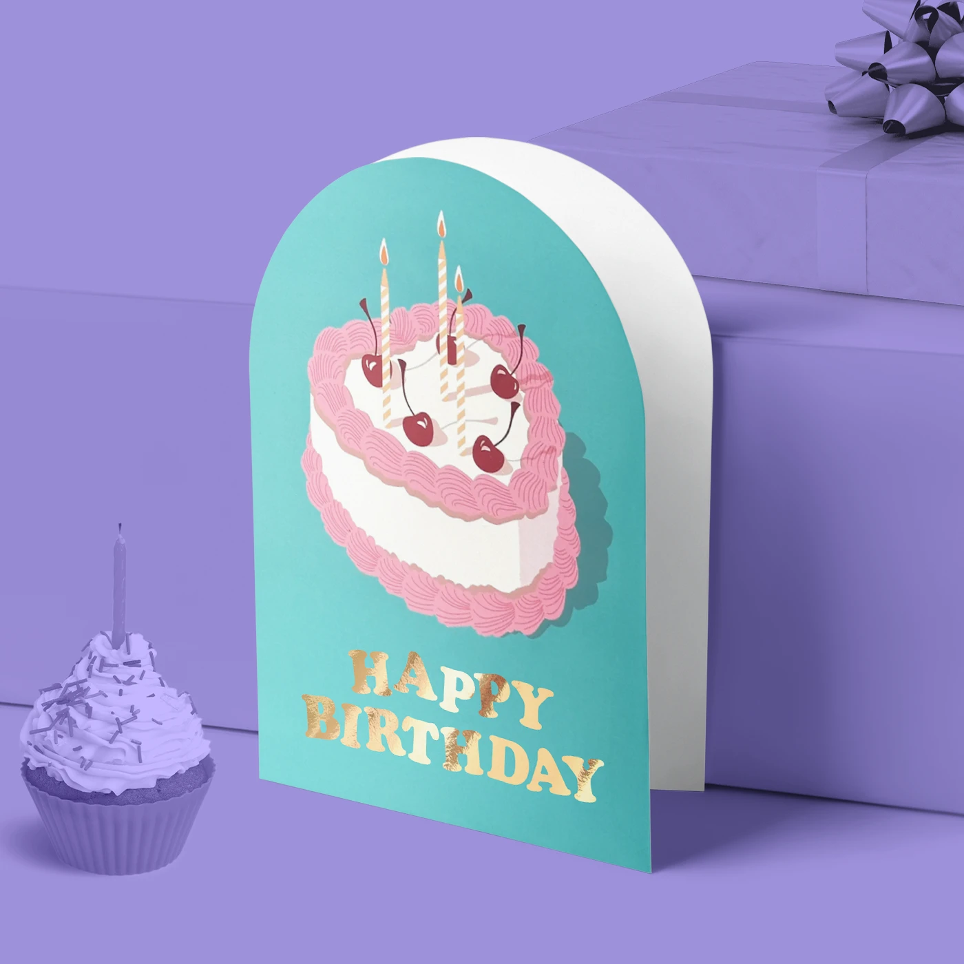 Arch shape Greeting Card with a blue background and a cake, with gold fold text reading 'Happy Birthday'. A purple background featuring a cupcake with candle and a wrapped gift box.