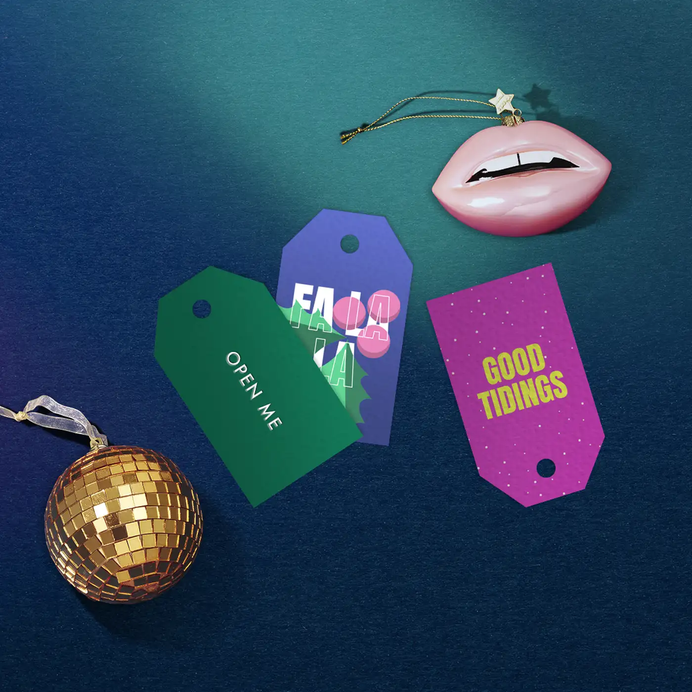 Three Christmas themed Gift Tags with pink, purple and green designs, placed on a dark blue background beside gold and pink Christmas ornaments.