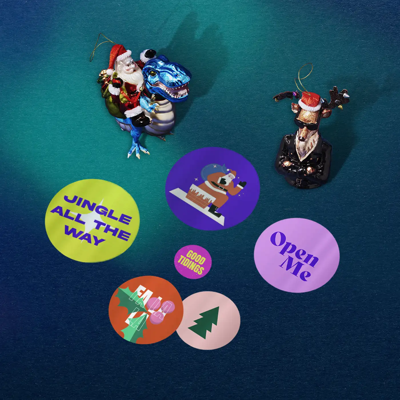 Various sizes of round Sticker featuring colourful Christmas designs, on a dark blue background beside two Christmas ornaments of santa and a reindeer,