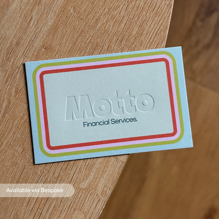 Blue rectangular business card on a wood background, featuring a debossed company logo outlined in red, pink, and green.