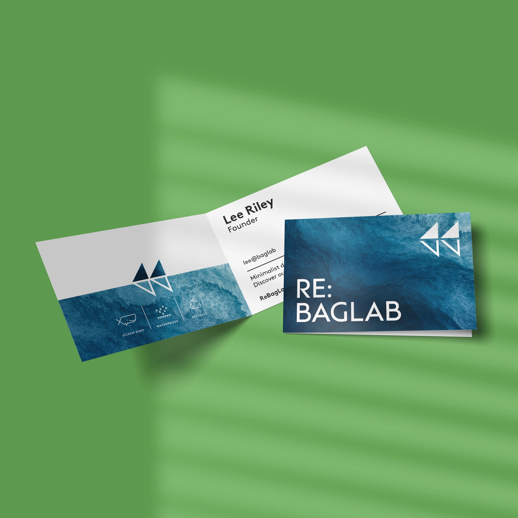 Two folded business cards on a green background, one open showing contact details and a brand logo and one closed showing the brand name in a white and blue design.