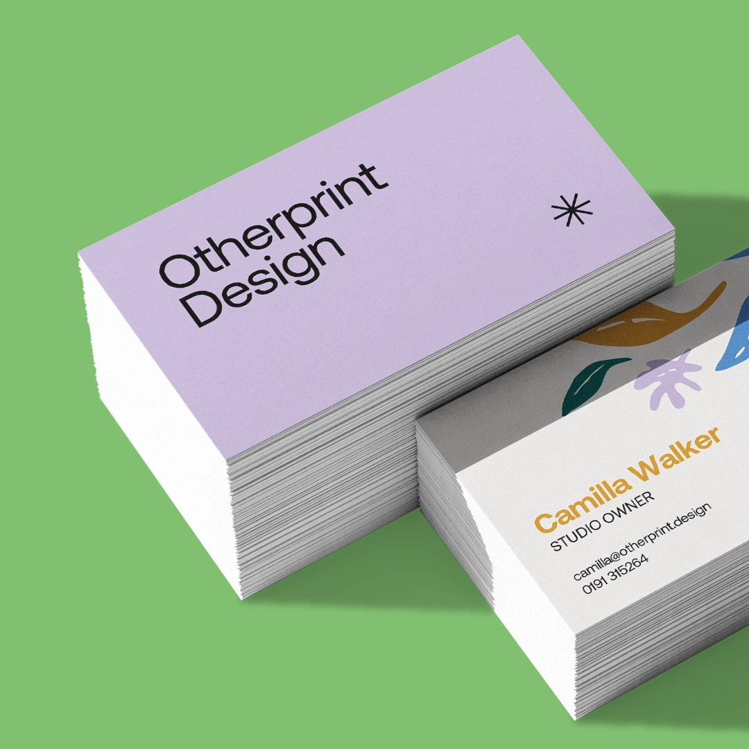 Two stacks of Business Cards on a green surface, showing a pale purple design with black text reading 'Otherprint Design' on one side, and a colourful design with contact details on the other side.