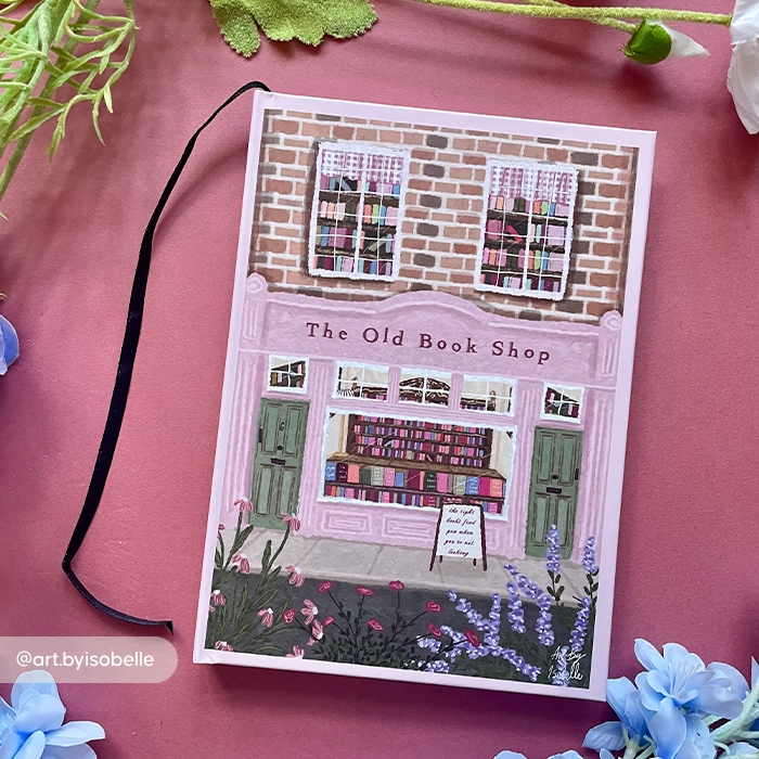 Hardback notebook with a whimsical illustration of a vintage bookshop, floral accents, and an inspiring quote.