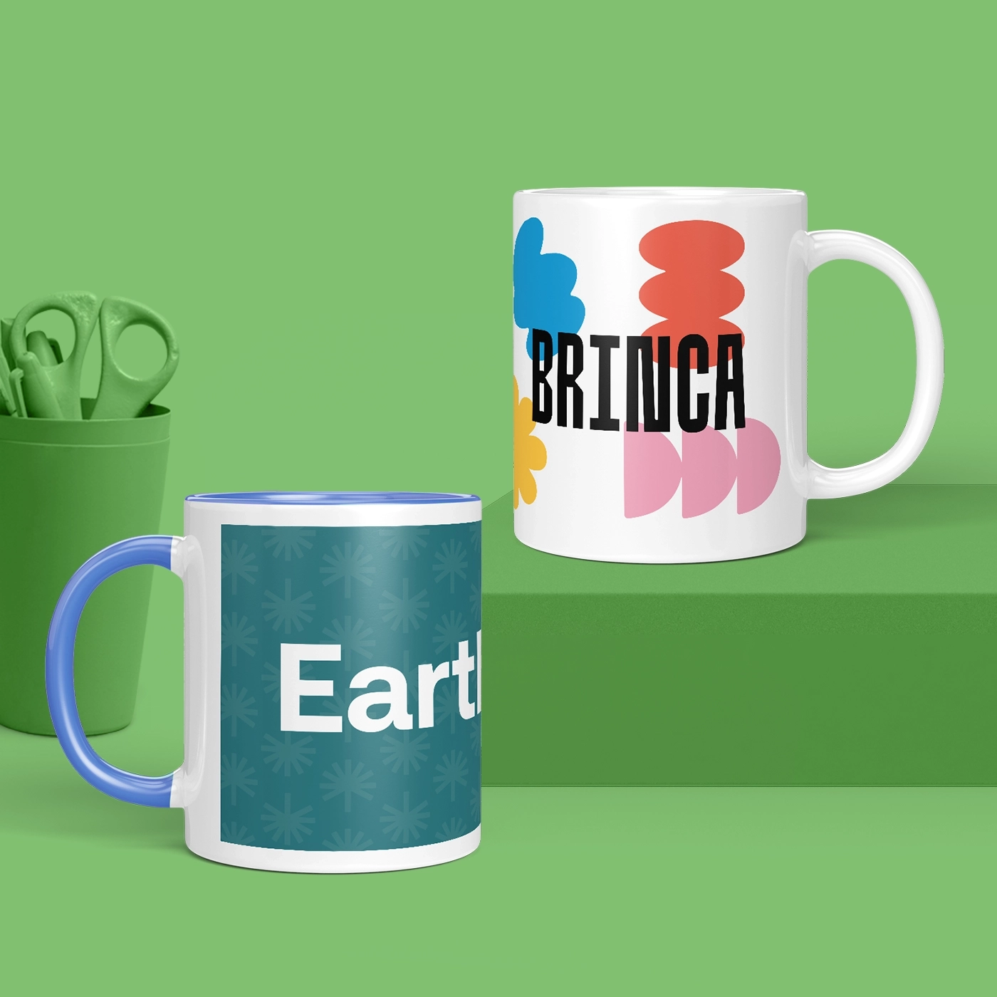 Two ceramic mugs displayed on green surface with matching green background and container of scissors.