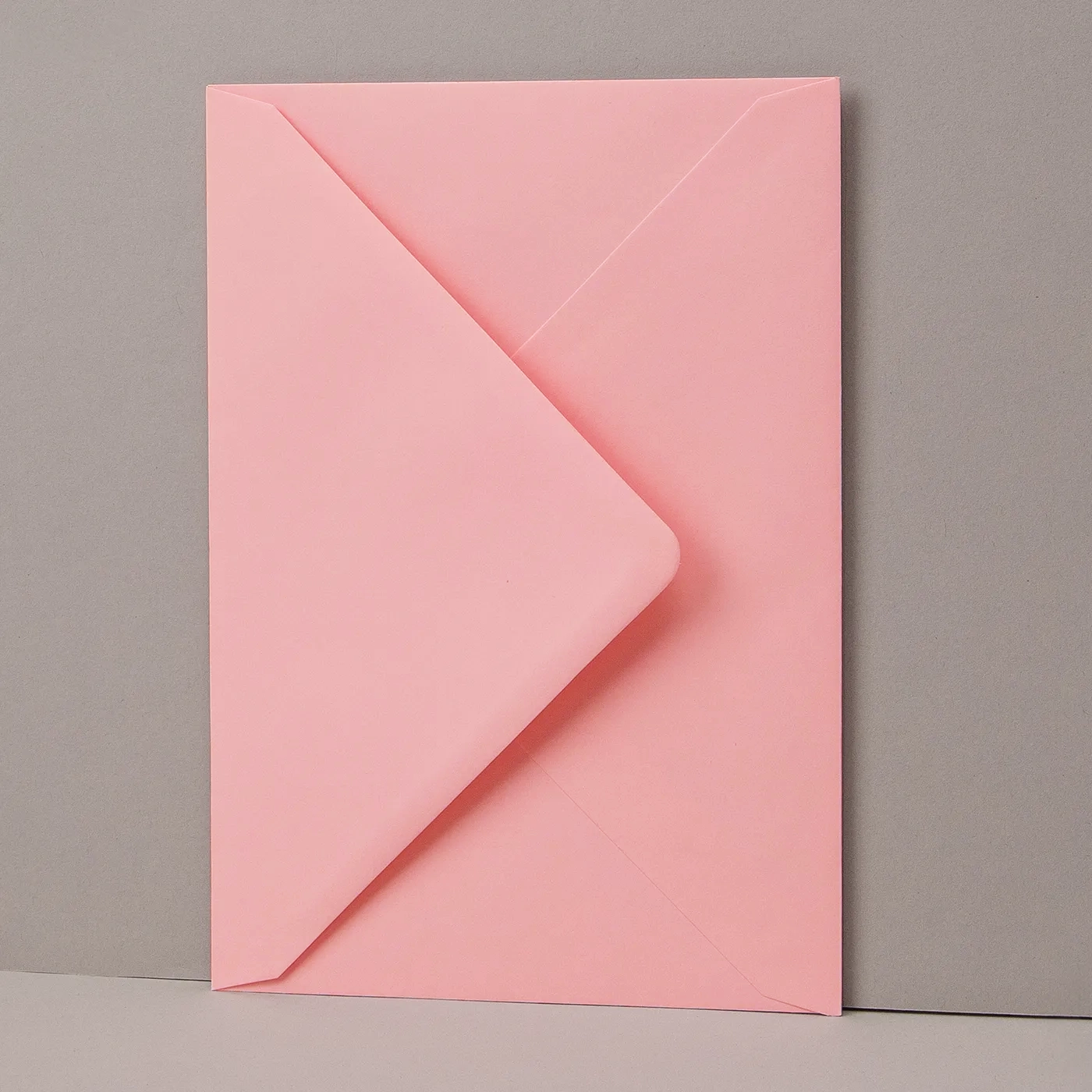 A light pink envelope vertically propped up on a grey background.