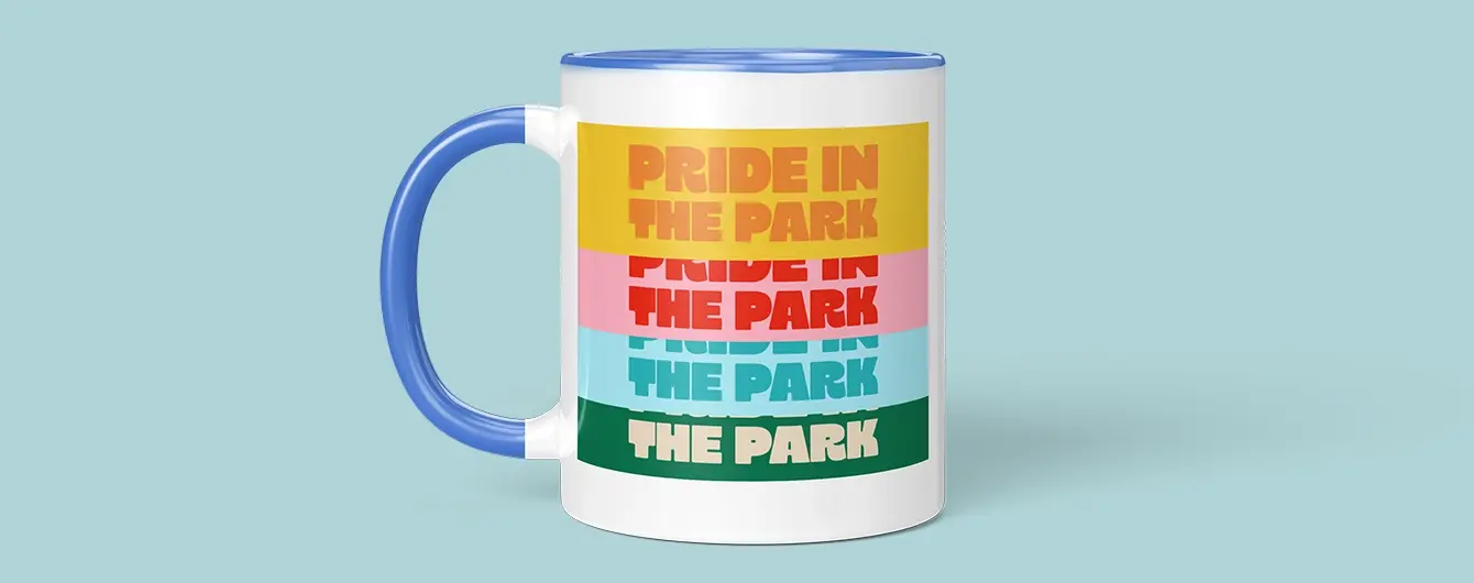 White mug with blue handle featuring stacked colourful text reading 'Pride in the Park' in multiple bold stripes.