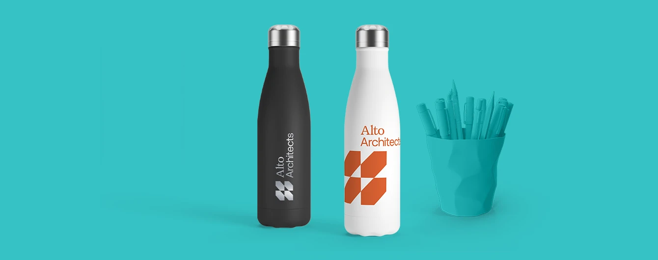 Two branded bottles and a pen pot with stationery, set against a turquoise surface and backdrop.