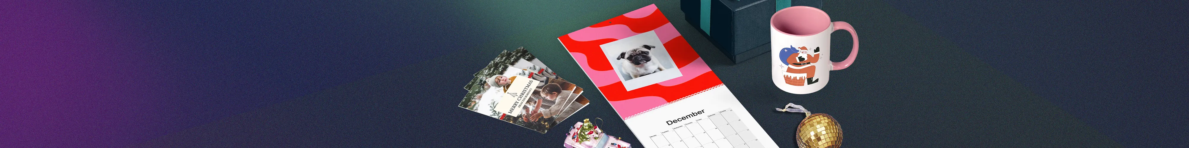 An range of printed Christmas gifts - a wall calendar open to December with a pug photo on the cover, a pink mug with an illustration, a small disco ball ornament, stacked gift boxes, and a fan of Christmas cards.