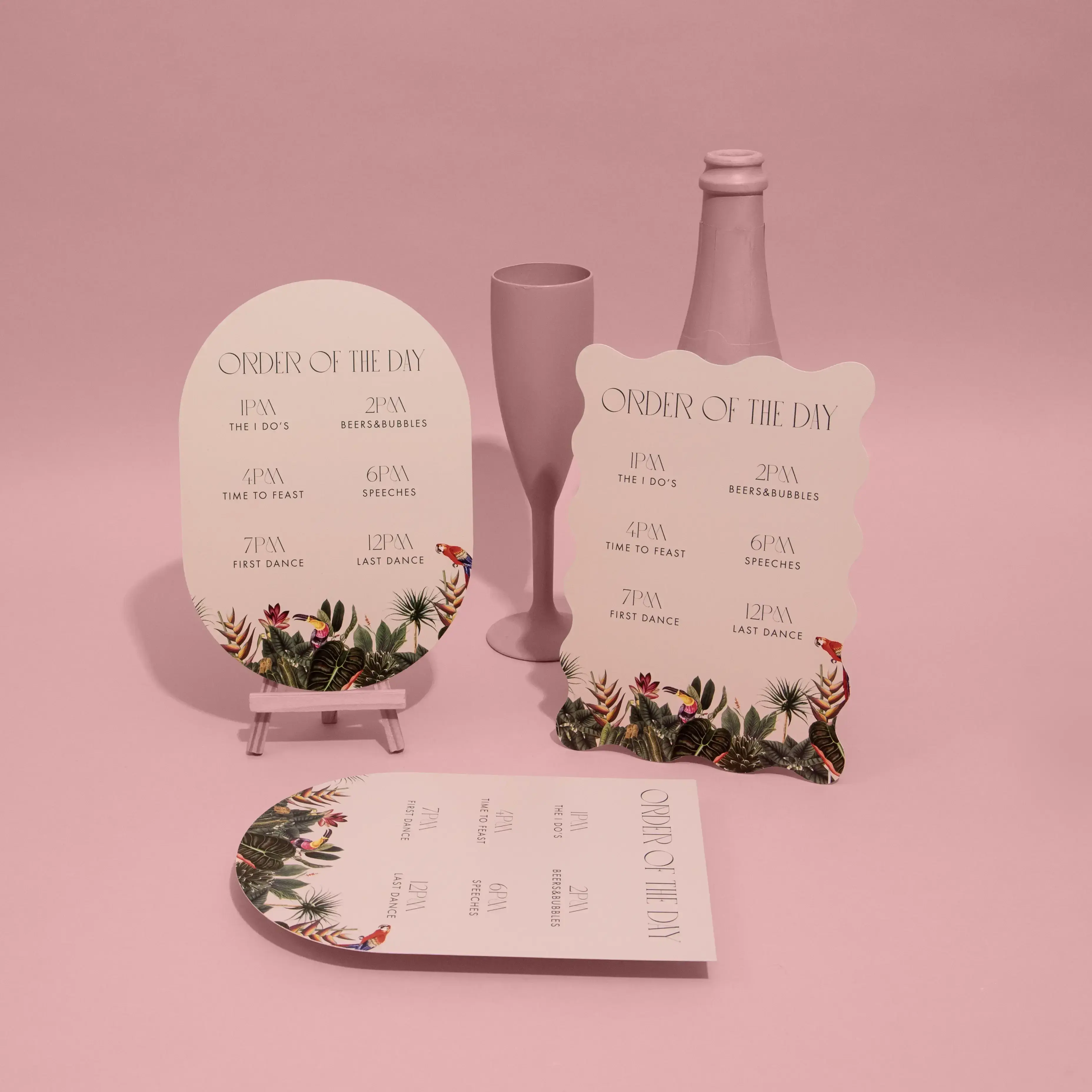 Set of pastel pink wavy and arch-shaped Wedding Order of Services, all with floral borders and printed wedding details, arranged on a pink background with a small pink vase.