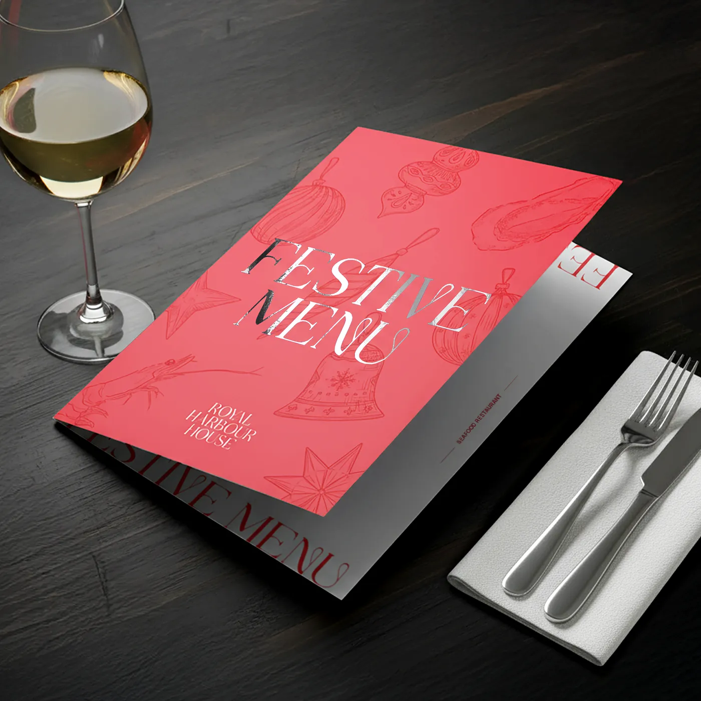Dining setup with red festive menu, wine glass, and silver cutlery on a dark wooden table.