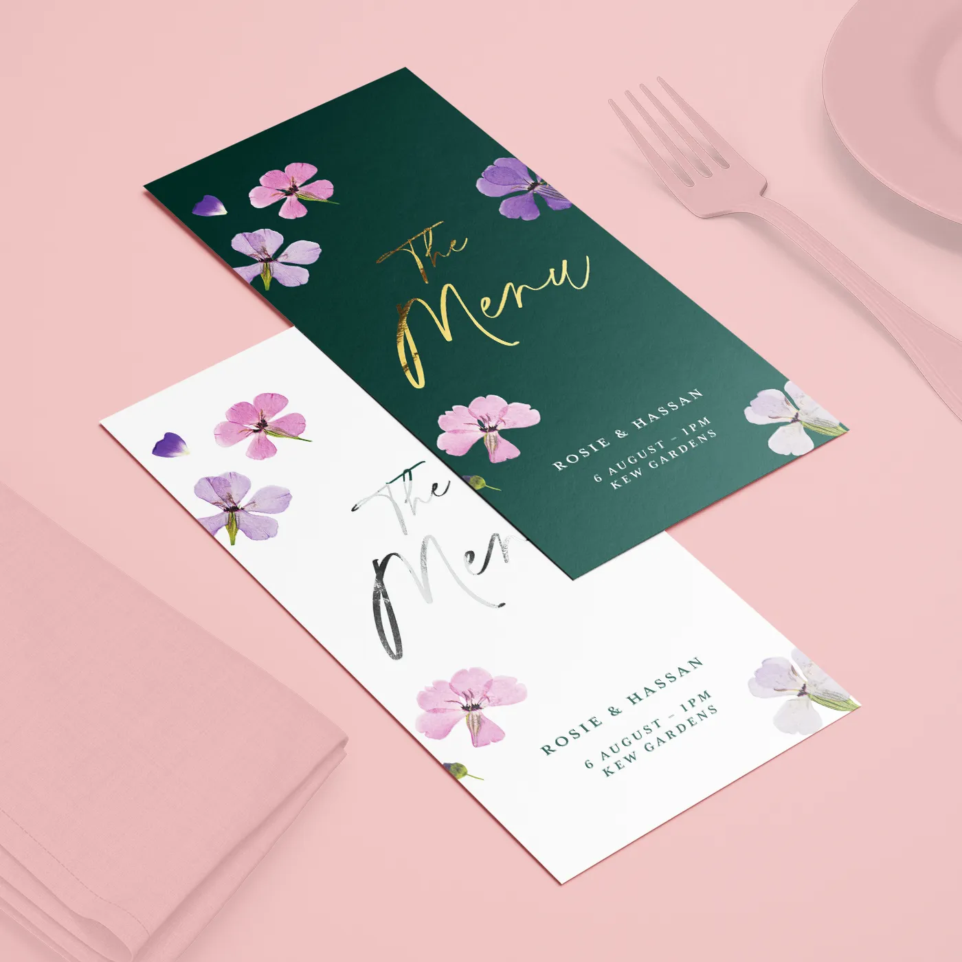 Menu cards with floral designs, arranged on pink tableware with matching napkin and cutlery.