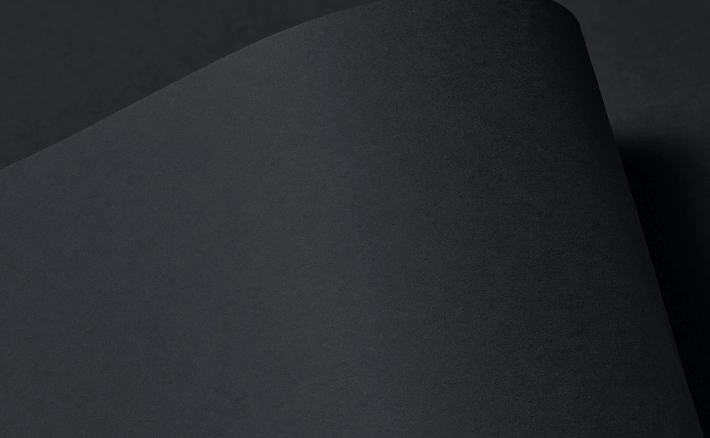 Close-up of Colourplan Ebony paper with a smooth, curved fold; the deep black surface has a refined matte texture, and the lighting creates subtle gradients that emphasize the material’s sculptural form and premium finish.