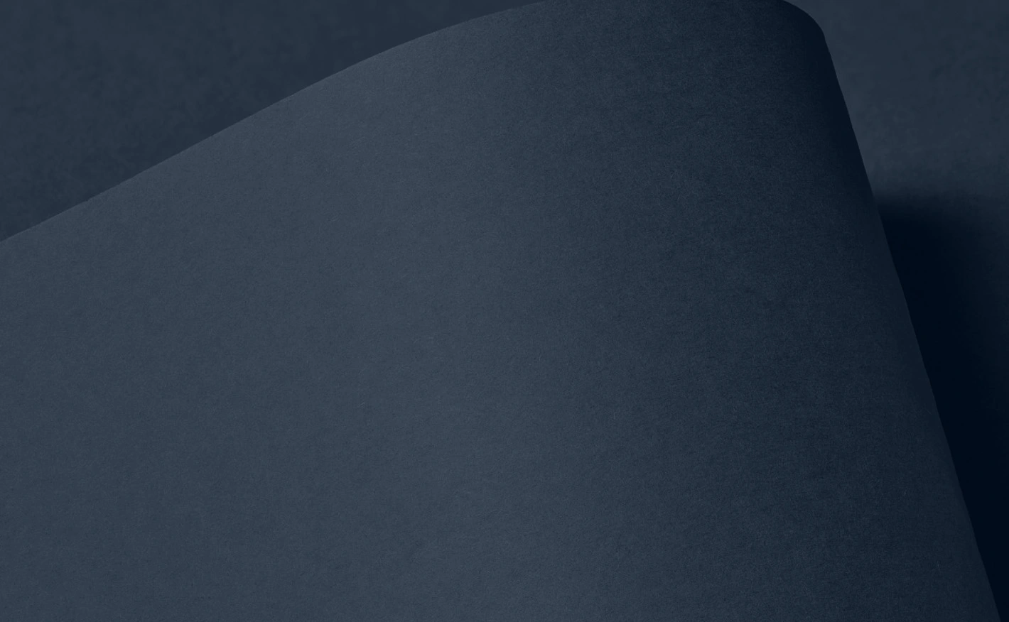 Close-up of Colourplan Loch Blue paper with a curved fold casting soft shadows; the surface has a rich, deep blue tone and subtle texture, emphasizing the premium quality and moody elegance of the material