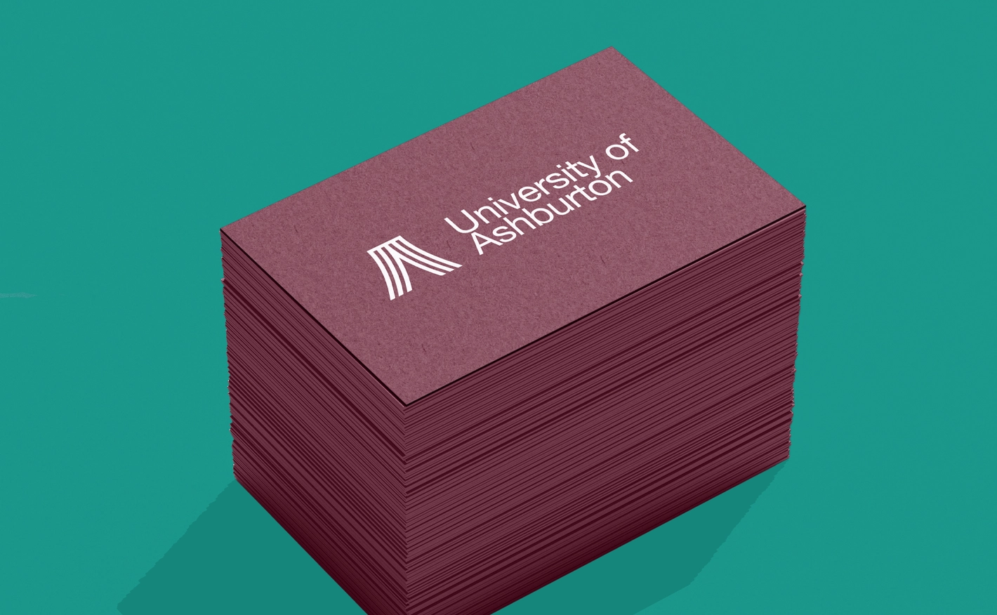Stack of maroon Business Cards on a teal surface; the top card features the University of Ashburton logo in white, with stylized lines beside the institution’s name, creating a clean and professional visual identity.
