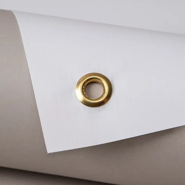 Rolled white vinyl with gold eyelet near edge, shown on a neutral grey background.