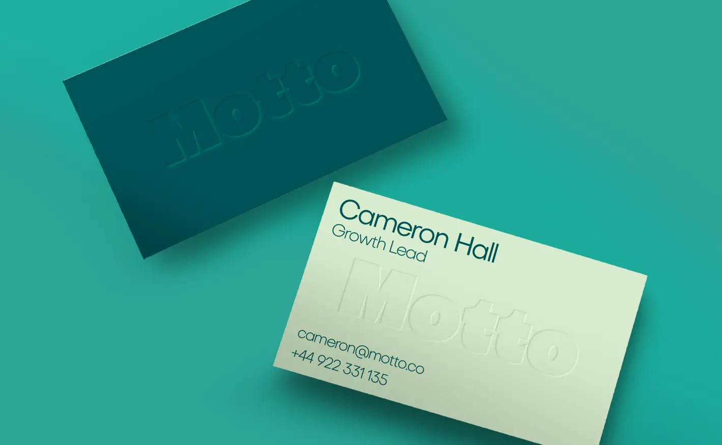 Two Business Cards on a teal background, both featuring embossed “Motto” branding, with contact details on one.