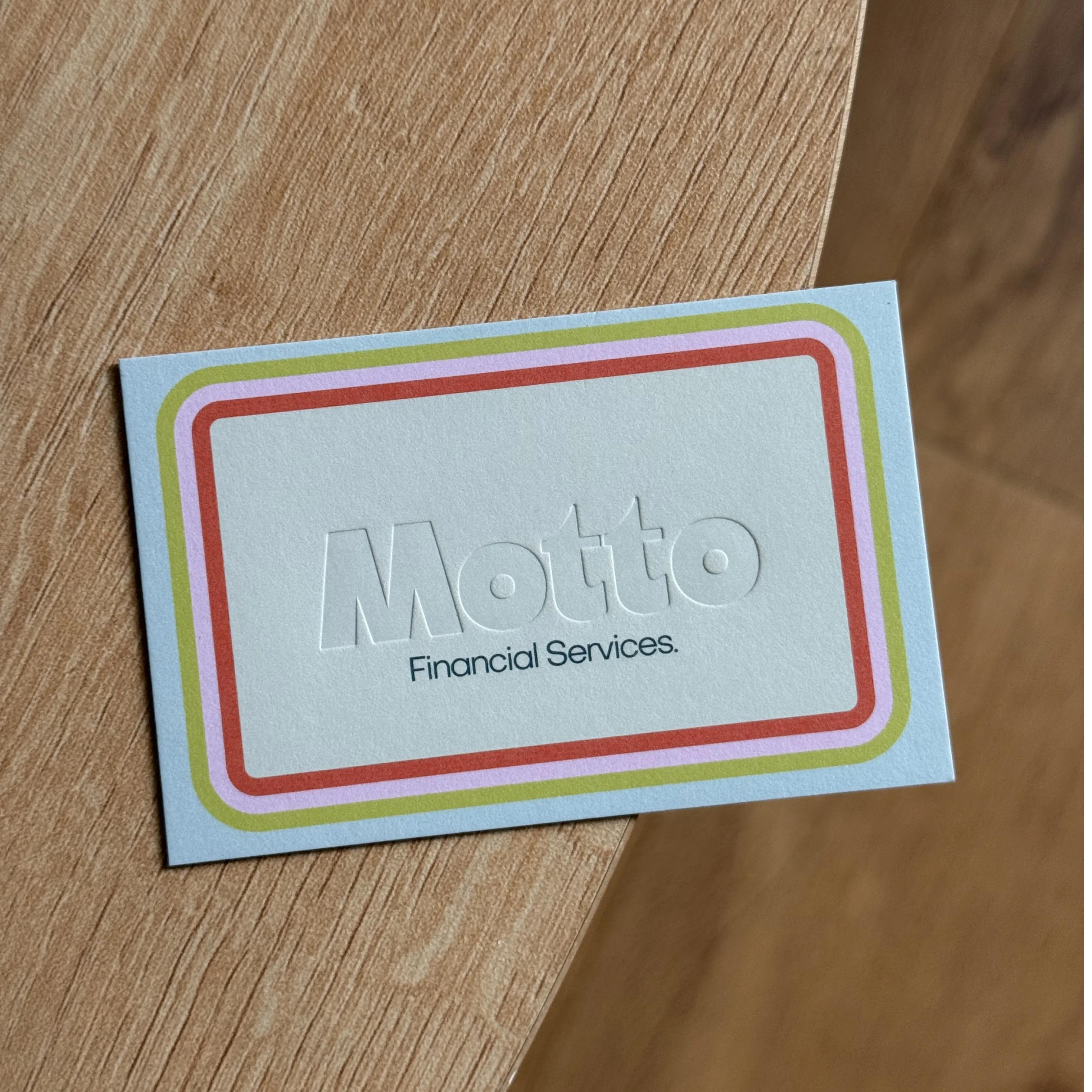 Debossed blue Business Card for Motto Financial Services, featuring a tri-colour border in green, yellow, and red