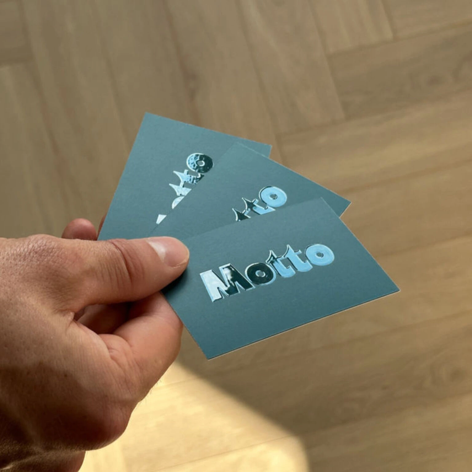 A hand fans out three blue Business Cards, each with the word "Motto" in Spot UV