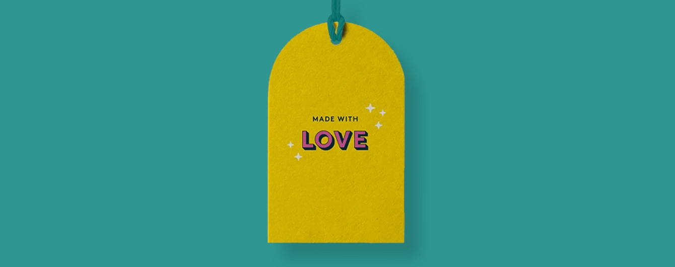 Yellow upper arch-shaped swing tag with green string, featuring the phrase 'MADE WITH LOVE' surrounded by small white sparkle illustrations.