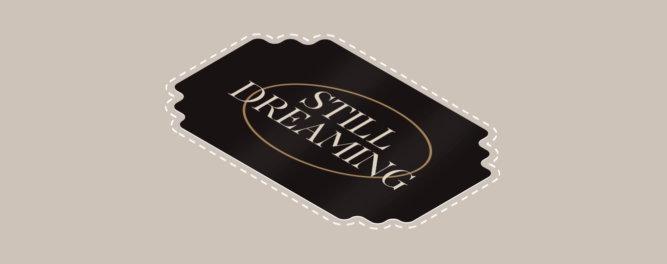 Black scalloped-edge sticker with a dashed white outline on a beige background. The ticket features the phrase “STILL DREAMING” in capital letters, encircled by a gold oval.