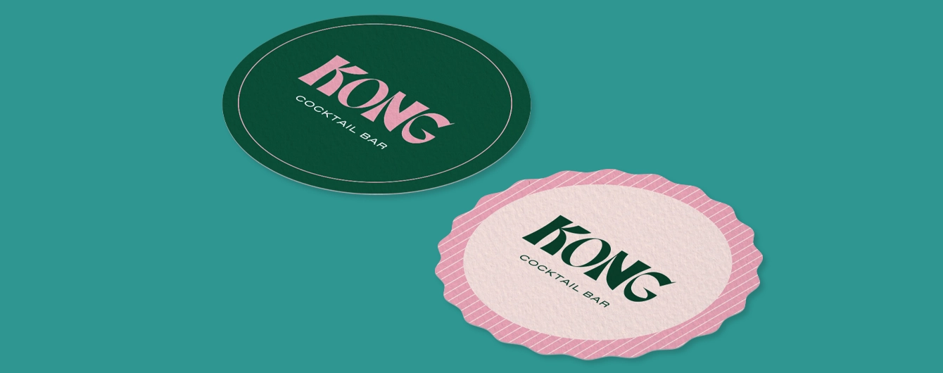 Two paper coasters - one pink wavy circle and one green circle. The text on both reads 'KONG Cocktail Bar'.