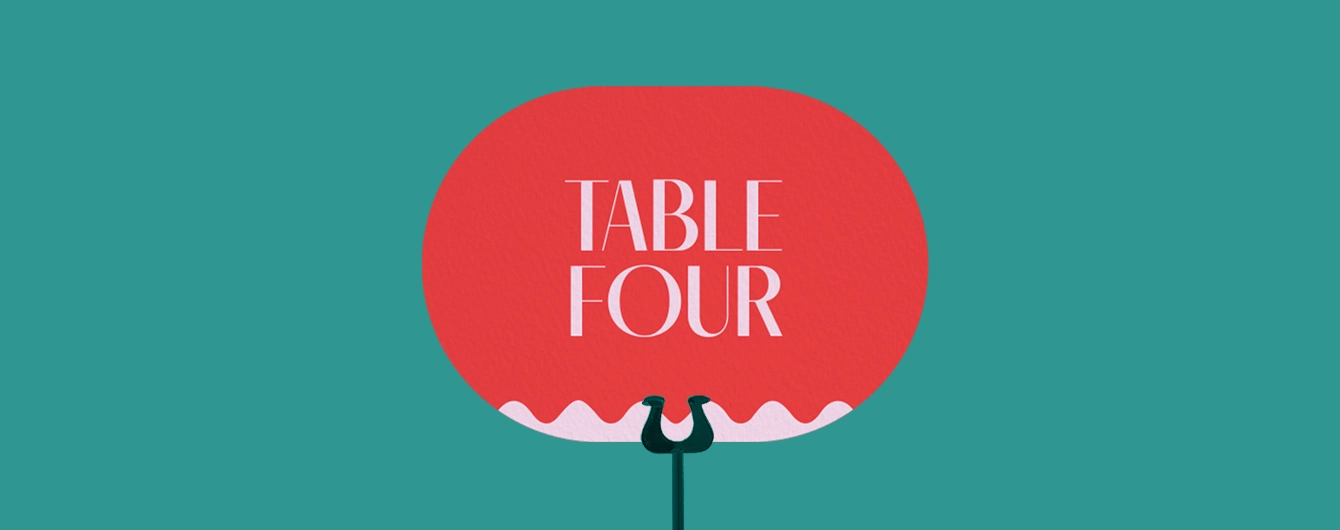 Red table name sign, mounted on a black stand. The sign reads 'Table Four' in bold letters.