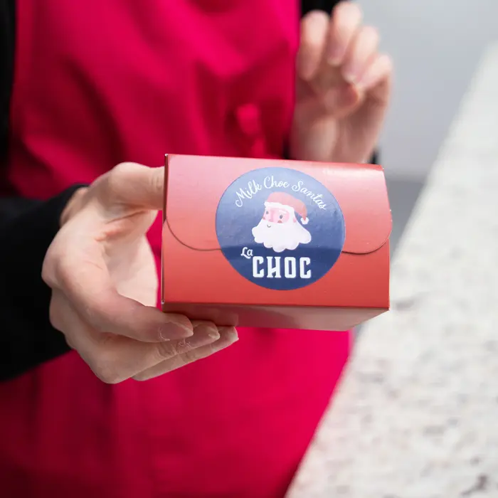 Round Sticker featuring a cheerful Santa Claus illustration with the text “Milk Choc Santa” and “La CHOC” in festive fonts, sealing a package