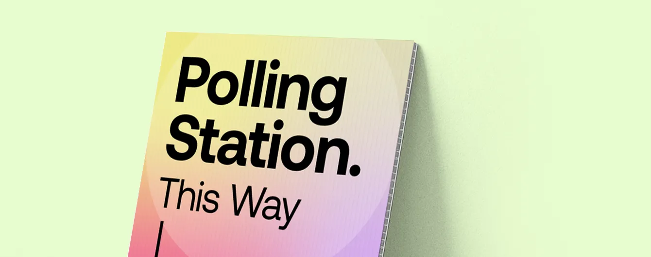 A close-up of a fluted Correx sign leaning against a pale green wall, featuring the bold text "Polling Station. This Way" against a yellow and pink gradient background.