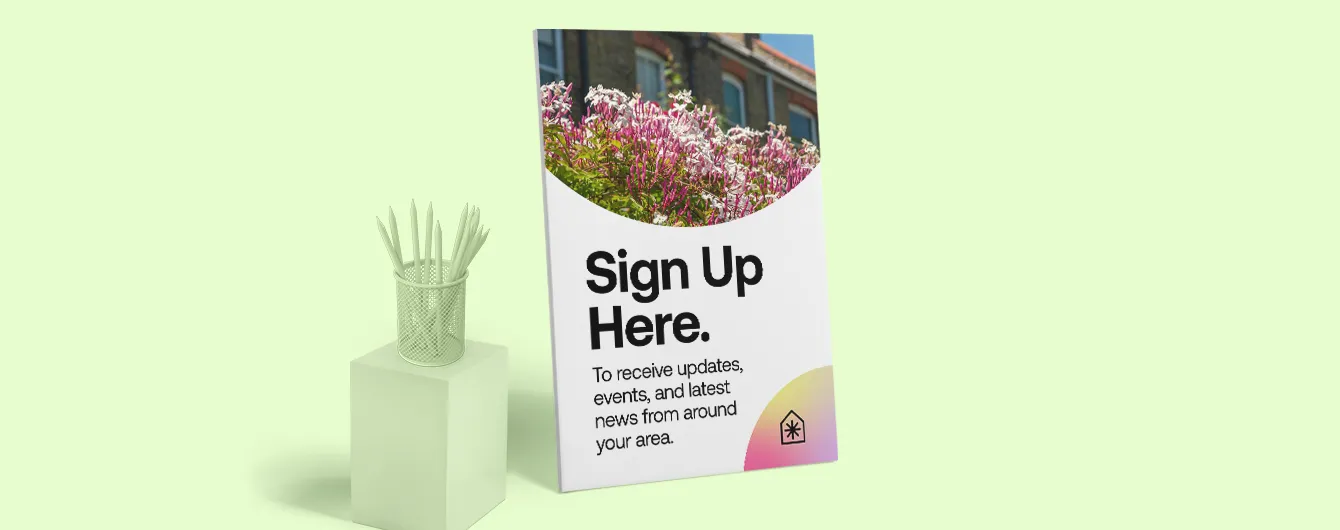 A large, free-standing foam board display propped against a light green wall, featuring a photo of pink flowers and the text "Sign Up Here" to encourage residents to receive local campaign updates and news.