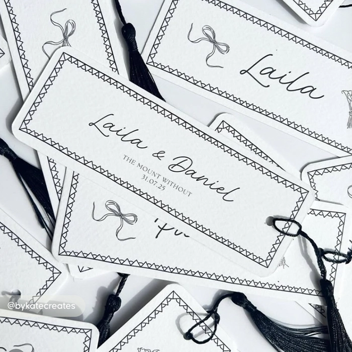 A pile of white wedding save the date Bookmarks with tassels attached