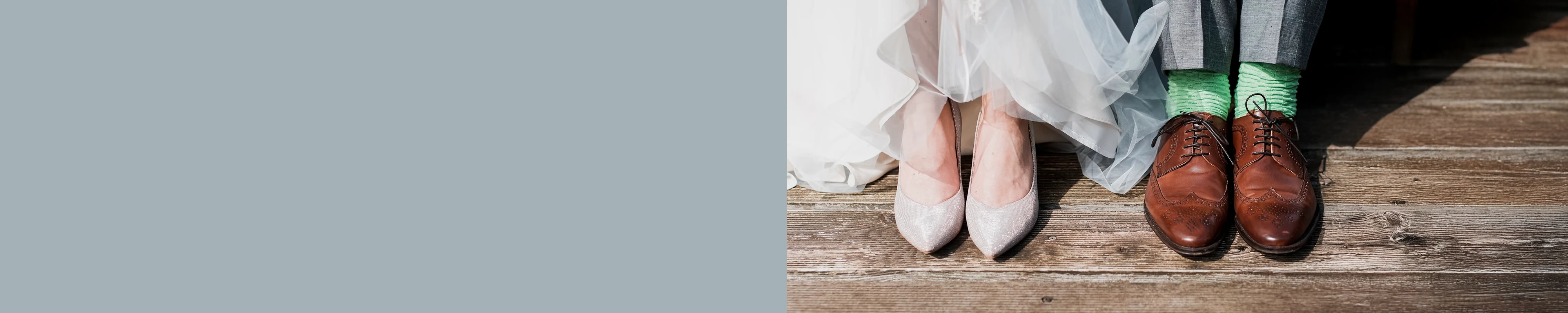 Close-up of a bride’s sparkly heels beside a groom’s brown shoes and patterned green socks, both standing on a wooden floor.