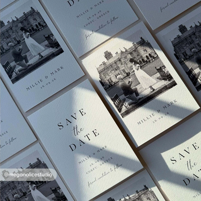 Flat‑lay arrangement of textured ‘Save the Date’ cards featuring a black‑and‑white proposal photo and the details ‘Millie & Mark, 10.09.24, Corfu, Greece.’