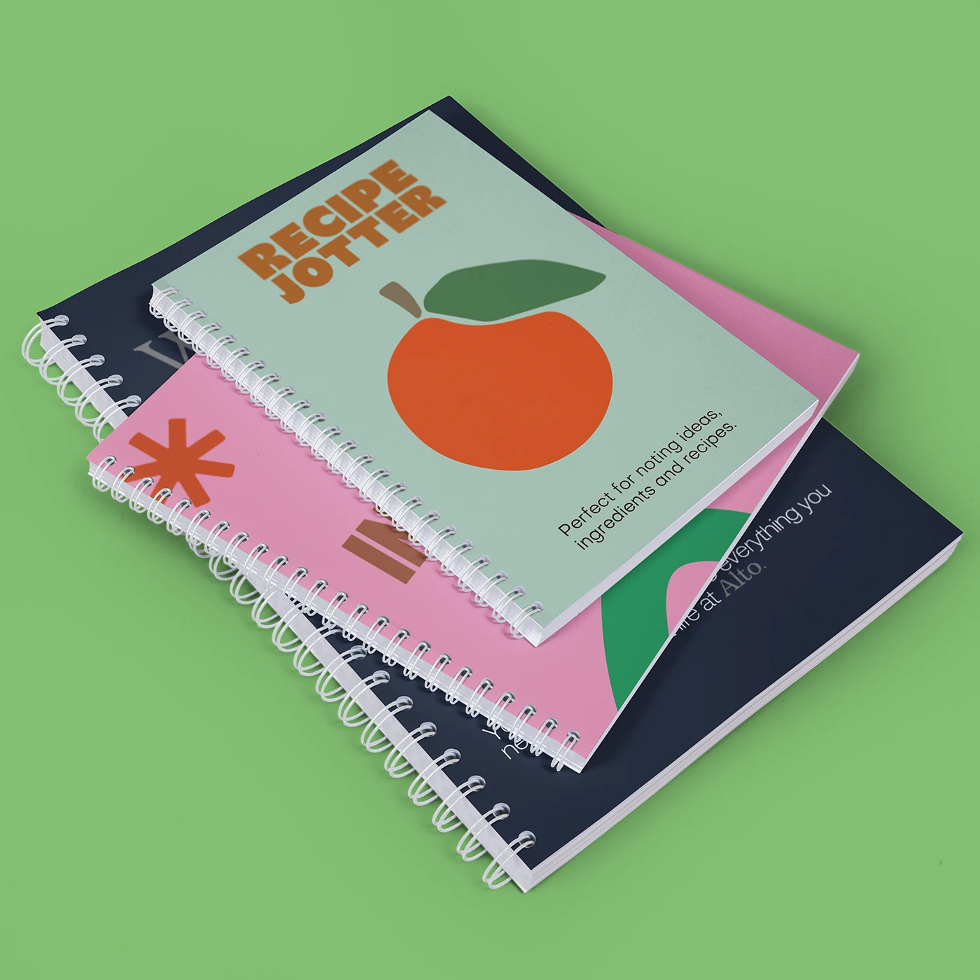 A stack of three Spiral Bound Notebooks: a light green ‘Recipe Jotter’ on top, a pink ‘Notes’ Notebook beneath it, and a dark blue Notebook partially visible at the bottom