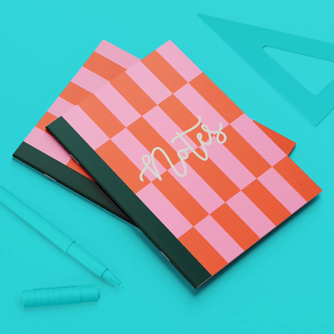 Two Saddle Stitch Notebooks with a pink and orange chequered cover, with a pen and triangular ruler placed beside them.