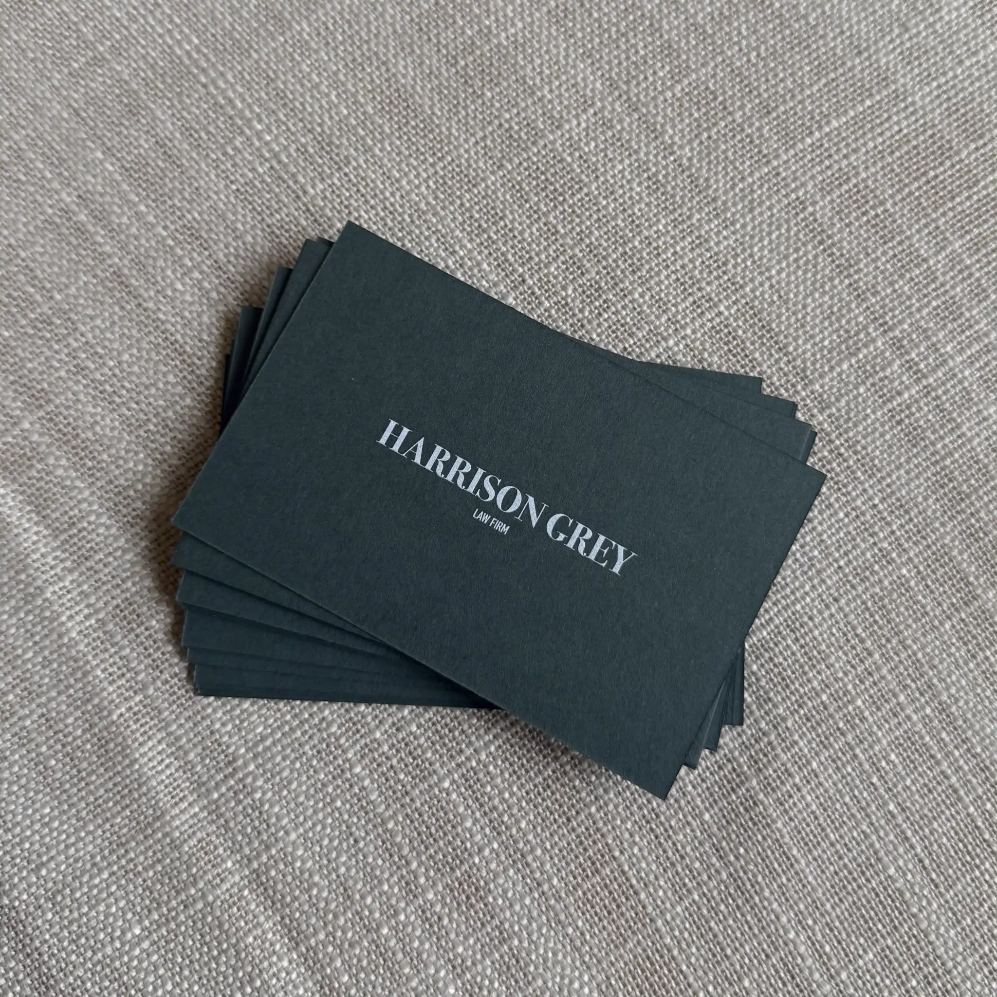 A stack of matte forest green business cards for "Harrison Grey Law Firm" features the company name printed in a crisp, elegant white ink serif font centred on the dark background.