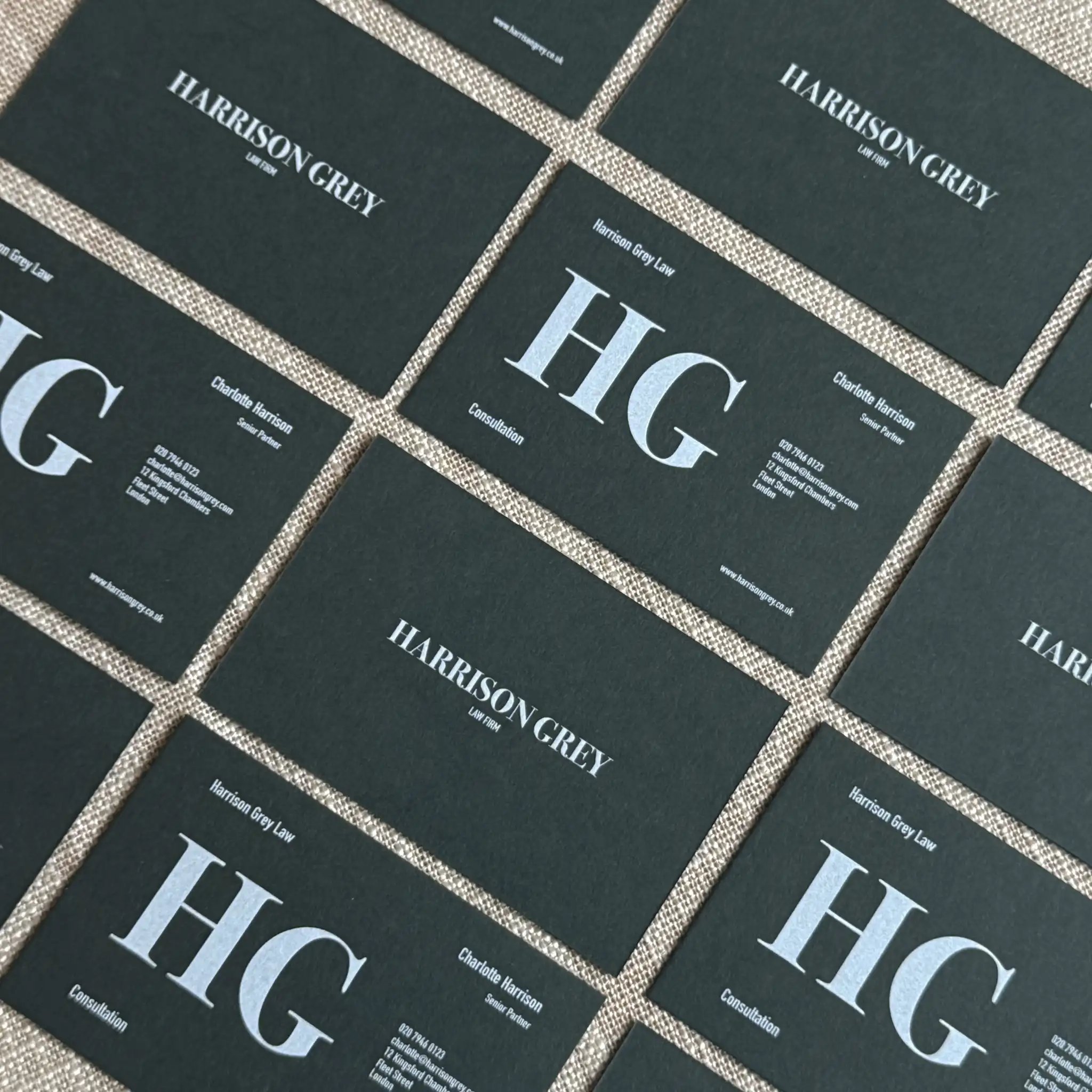 An overhead grid of forest green business cards for "Harrison Grey Law Firm" showcases crisp white ink printing, using a combination of large, bold monogrammed initials and small, legible contact details.