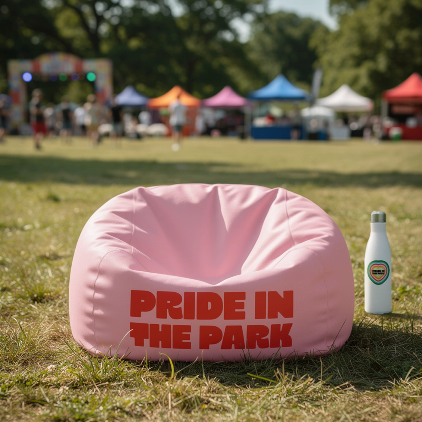 Pink bean bag on grass with matching bottle, tents, and festival crowd behind.