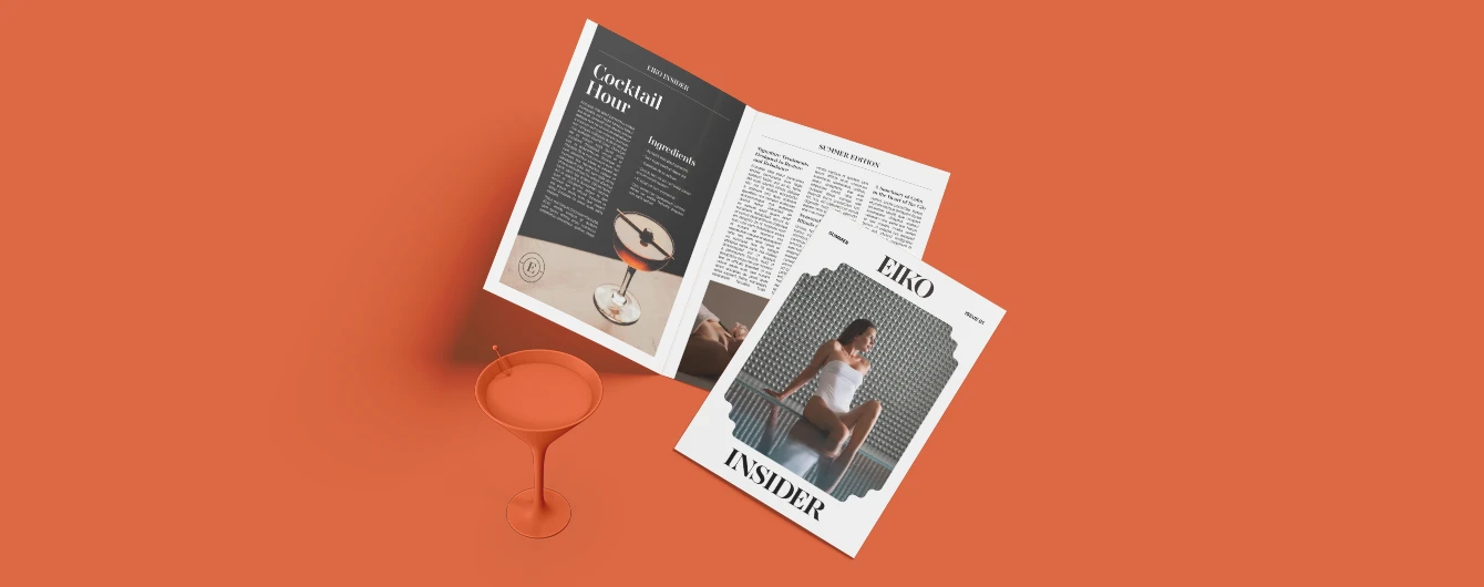 Lifestyle newspaper opened on a vibrant orange background with a matching cocktail.