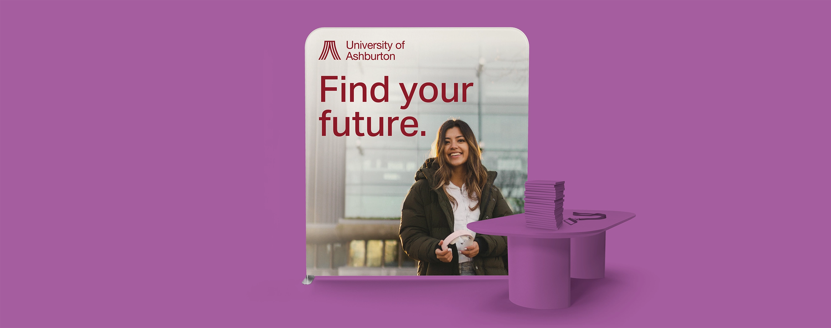 A stretch fabric display stand for a university open‑day setup with a table on a purple backdrop.