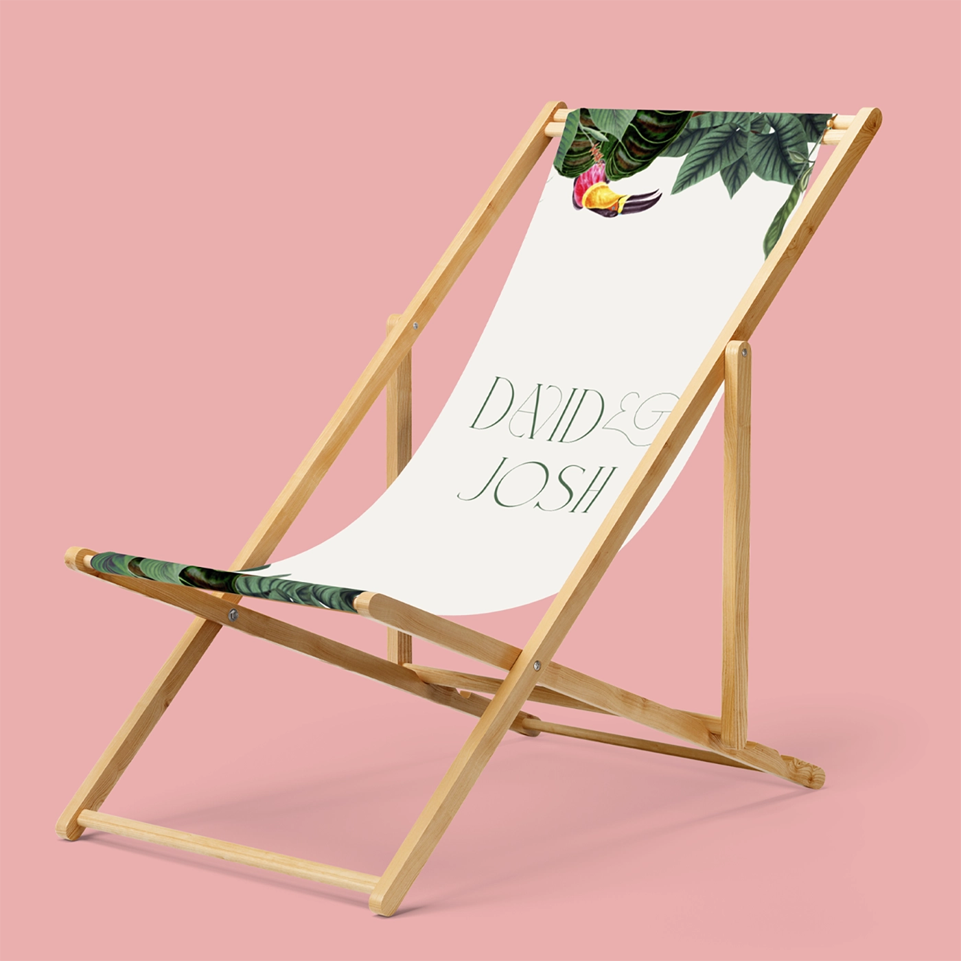 A wooden Wedding Deck Chair with a pink fabric seat featuring tropical leaves and flowers, personalised with the names ‘David & Josh’ in decorative lettering.