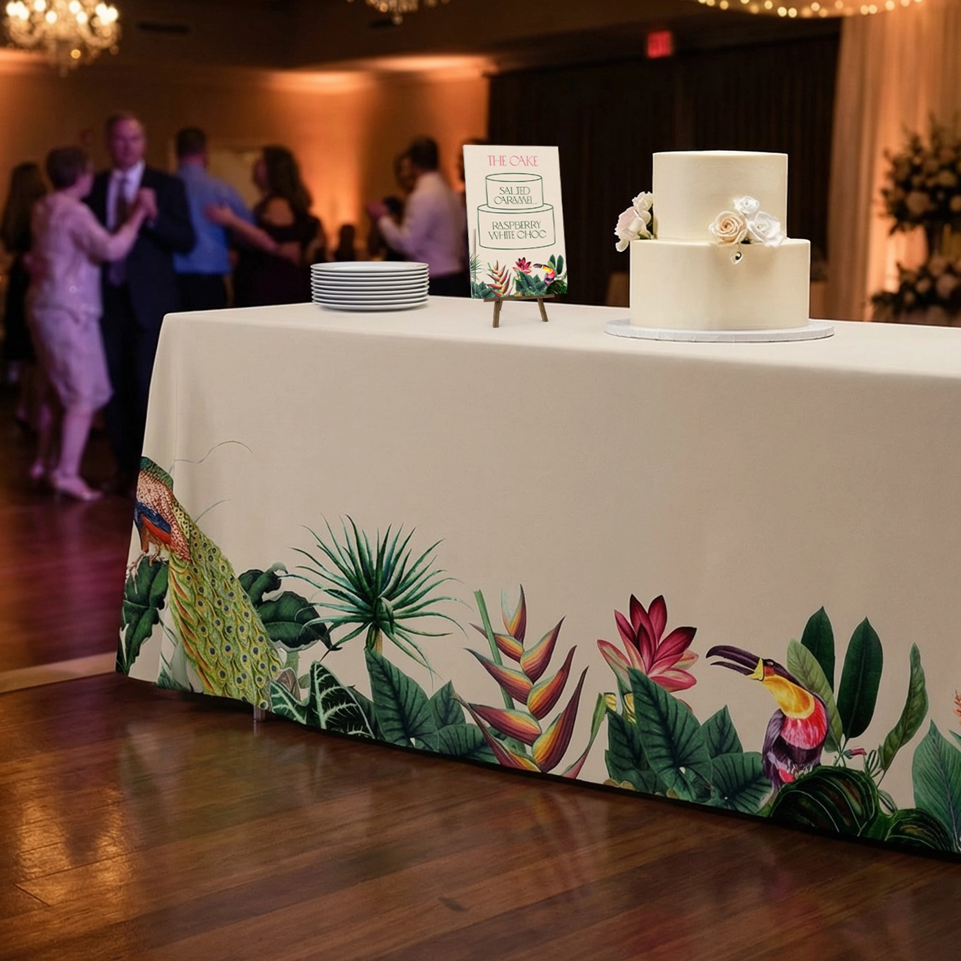 Decorated rectangular table with a patterned tablecloth at a lively wedding reception.