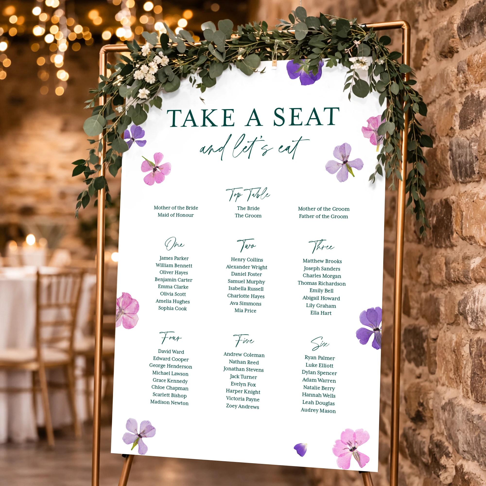 A white Wedding Table Plan Poster titled "TAKE A SEAT and let's eat," decorated with purple floral illustrations and displayed on a gold frame with greenery, in a brick wall reception setting.