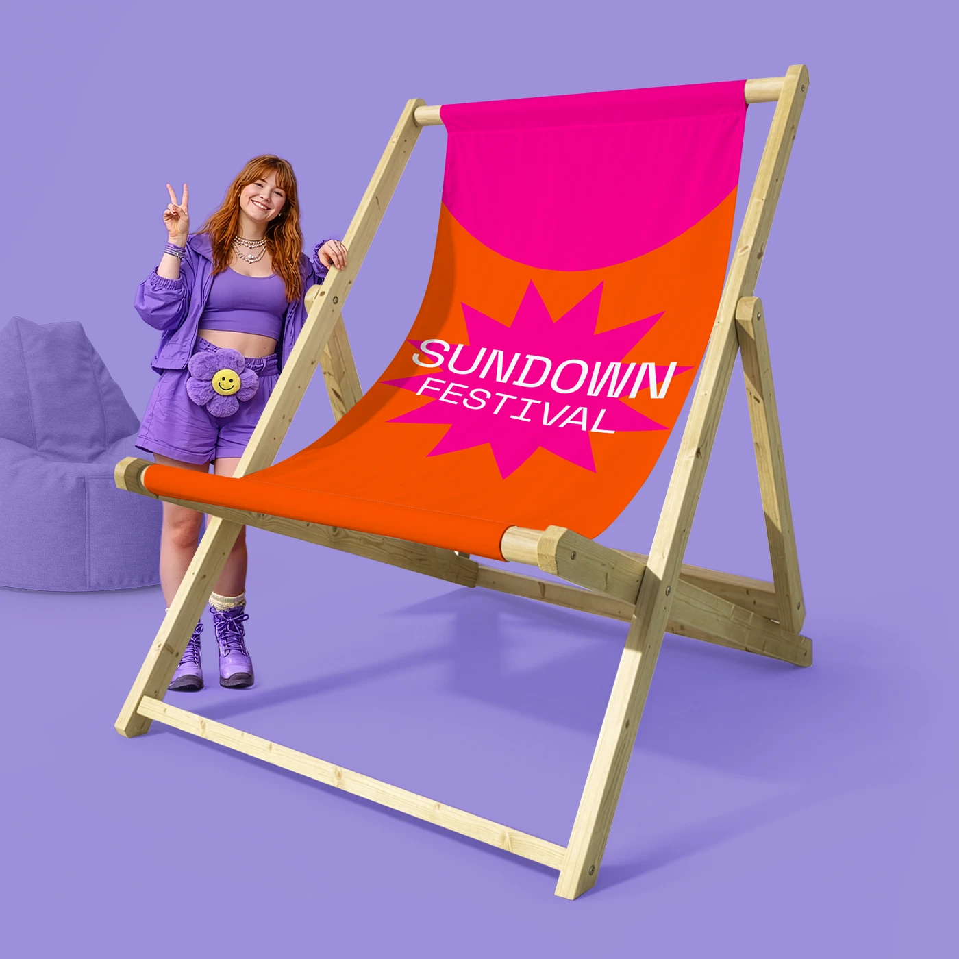 A bright giant deck chair with a person posing beside it against a colourful backdrop.