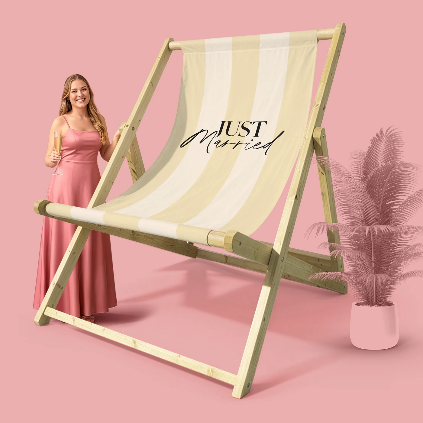 A woman in a pink dress standing beside a giant striped deck chair on a pink backdrop.