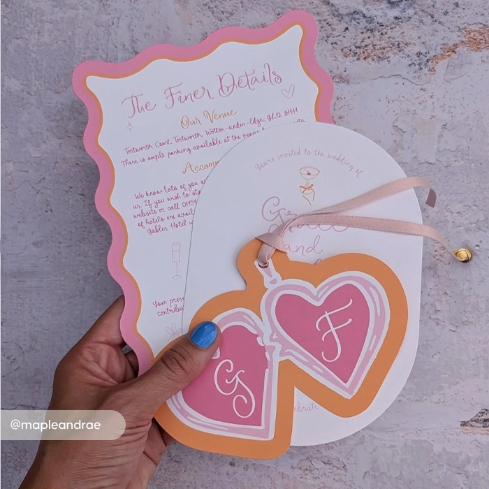 Retro-style wedding invitation suite featuring a pink scalloped "Finer Details" card and a heart-shaped monogrammed tag tied with a pink ribbon.