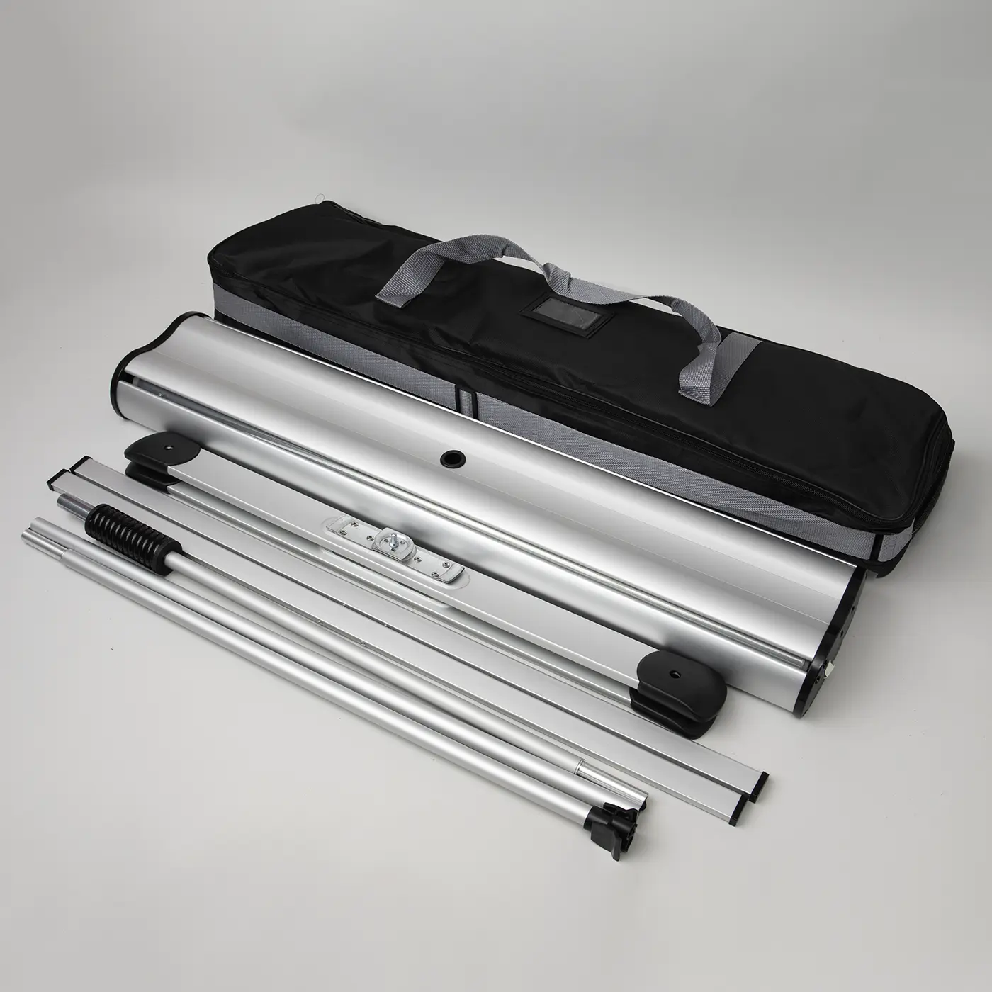 Silver Outdoor Roller Banner hardware set featuring a wide aluminium base, heavy-duty support poles with spring tensioners, and a black padded carry bag with grey straps.
