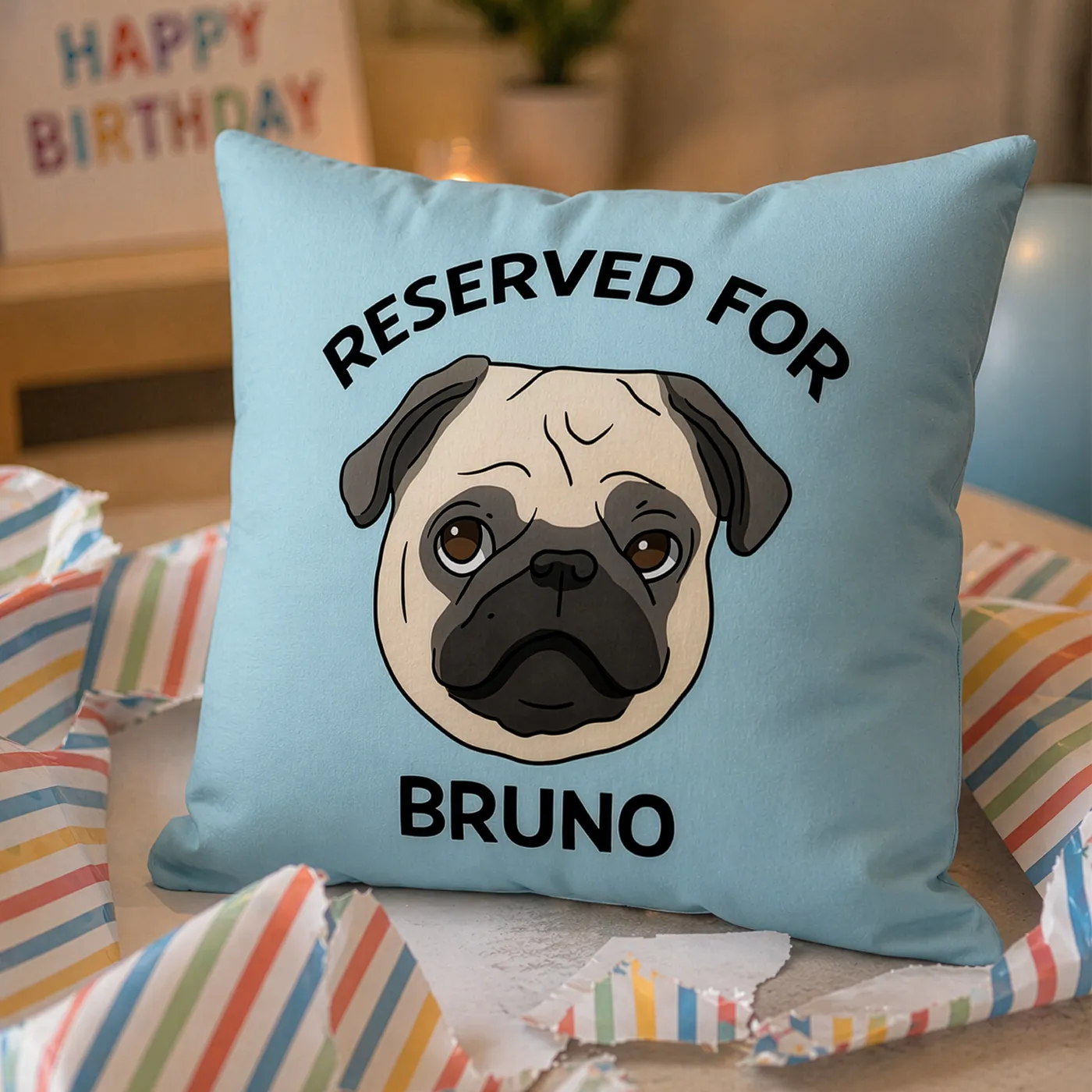 A blue Personalised Pet Illustration Cushion featuring a drawing of a pug, next to unwrapped paper suggesting a birthday gift.