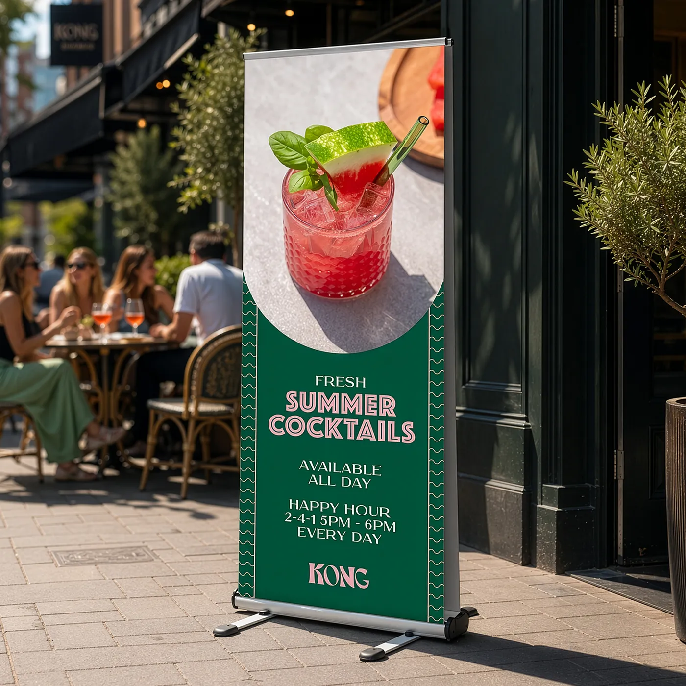 An Outdoor Roller Banner for "Kong" featuring a green and pink design with a photograph of a watermelon cocktail and text advertising "Fresh Summer Cocktails" and "Happy Hour."