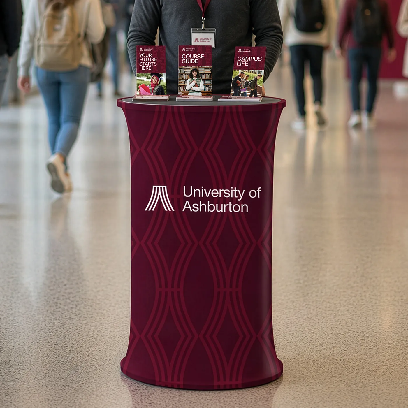 An oval Pop Up Counter for the University of Ashburton featuring a maroon geometric pattern and university brochures on the tabletop.