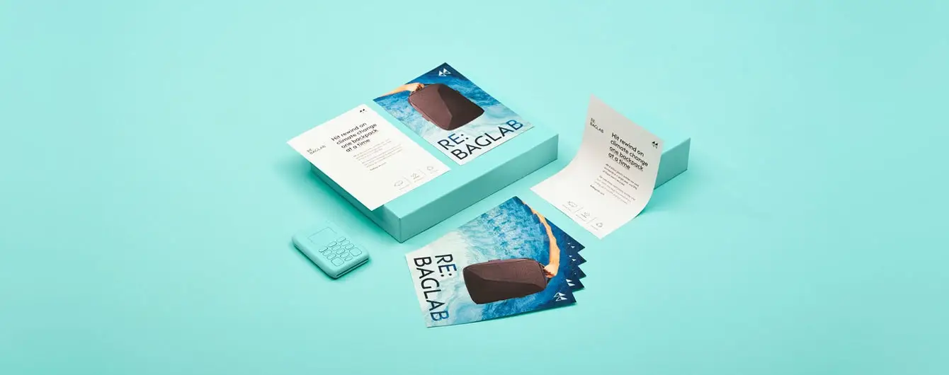 A collection of marketing leaflets for 'RE: BAGLAB' featuring water imagery and a brown backpack design, arranged on a light teal background alongside a matching card payment terminal.